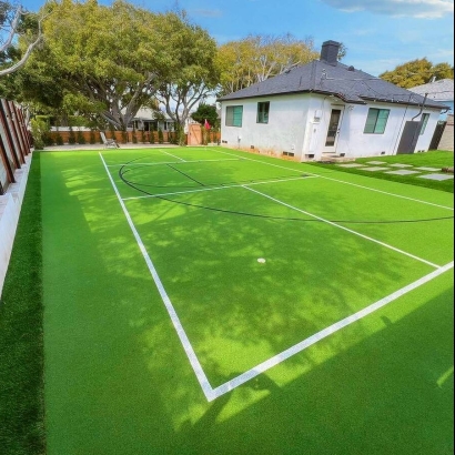 A residential backyard with a tennis court covered in artificial grass and surrounded by trees.