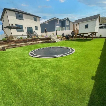 A backyard with artificial turf, featuring an in-ground trampoline and surrounded by modern houses. Super Natural Lite.