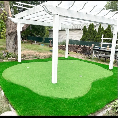 A small backyard putting green under a white pergola, surrounded by artificial grass.