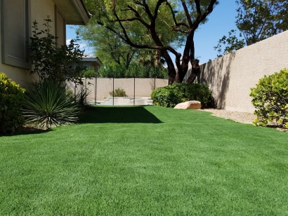 Backyard synthetic lawn artificial grass installation green landscape with shrubs by stone fence Riviera Monterey 50 M Blade shape blades