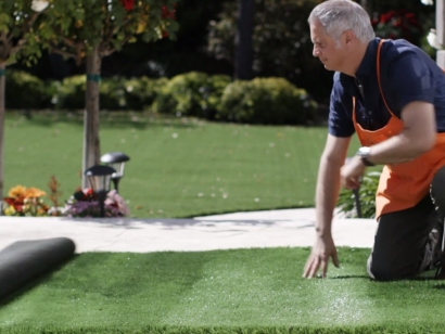 man laying down artificial grass on a patio