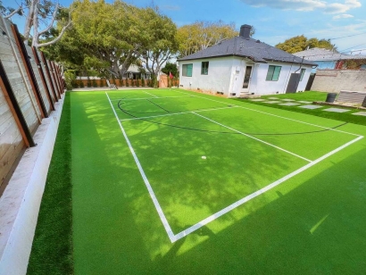 A residential backyard with a tennis court covered in artificial grass and surrounded by trees.