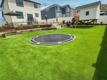 A backyard with artificial turf, featuring an in-ground trampoline and surrounded by modern houses. Super Natural Lite.