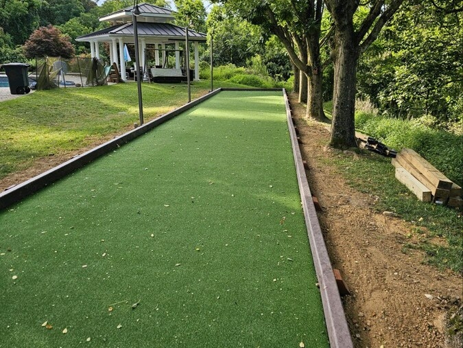 A bocce ball court with artificial turf and a gazebo in the background, lined with trees Maryland