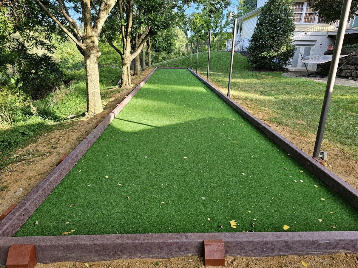 A bocce ball court covered in artificial turf, surrounded by trees in a backyard setting. Maryland