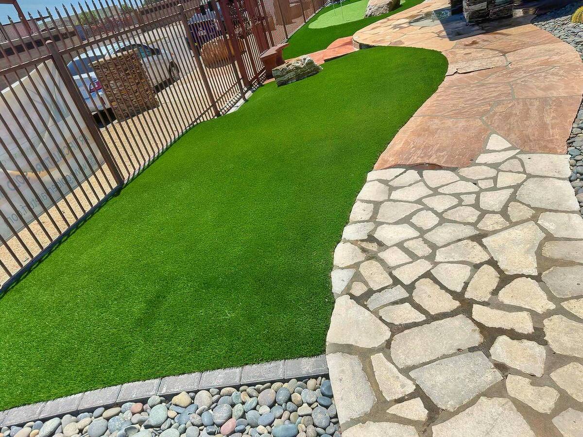 A pathway of artificial turf alongside a stone walkway and decorative rocks.