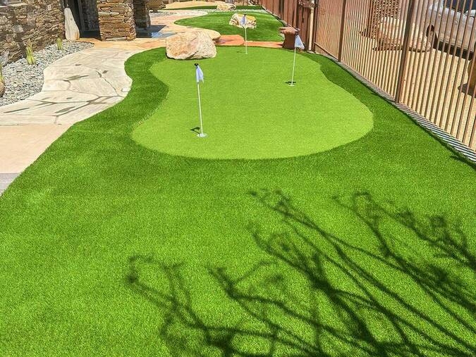 A putting green made of artificial turf adjacent to a building with a stone facade.